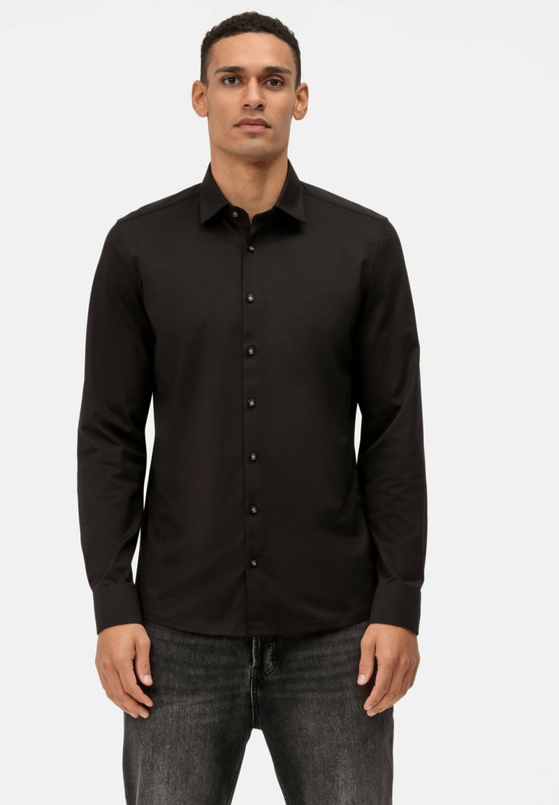 Schwarzes, langärmliges Hemd mit Knopfleiste und Kragen, schlichtes Design und schwarzen Knöpfen, kombiniert mit dunklen Jeans. Glatte Stoffstruktur.