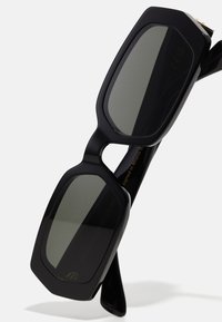 Mustad mustad prillid tumedate läätsedega, paksu raami ja nurkse kujundusega. Textuuriga varred kuldse detailiga, minimalistlik brändimine.
