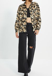 Camicia floreale a maniche lunghe nera, beige e crema, abbinata a jeans neri a vita alta con un ginocchio strappato. Stivaletti neri completano il look.