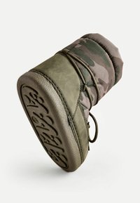 Botte vert olive avec un dessus en tissu matelassé à motif camouflage. Dispose d'une semelle en caoutchouc texturée et d'un système de laçage pour un maintien sécurisé.