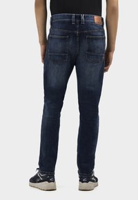 Jeans en denim bleu foncé avec une coupe slim, dotés de deux poches arrière, de coutures contrastées et d'un patch en cuir sur la ceinture.