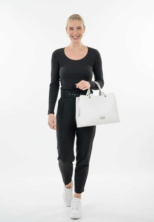 Maglietta nera a righe con maniche lunghe, pantaloni neri a vita alta, borsa bianca con finiture in argento e sneaker bianchi. La modella è in piedi davanti a uno sfondo bianco.