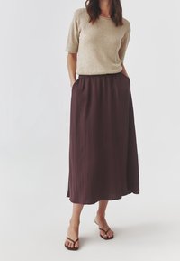 Top corto beige de punto con manga corta y cuello redondo, combinado con una falda midi fluida en tono burdeos oscuro. La modelo lleva chanclas marrones.