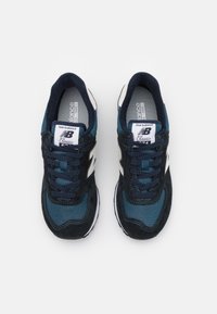 Ett par marinblå och svarta New Balance Classic 574-sneakers med vit "N"-logotyp och snörning, vy ovanifrån på en ren vit bakgrund.