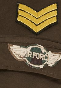 Militäruniform-patch med en brun tygbakgrund, guldchevrons och en broderad "Flygvapen"-insignia med vingar.