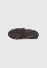 Black rubber shoe sole with textured grip pattern and round logo. Features a raised circular detail near the heel and flat profile.