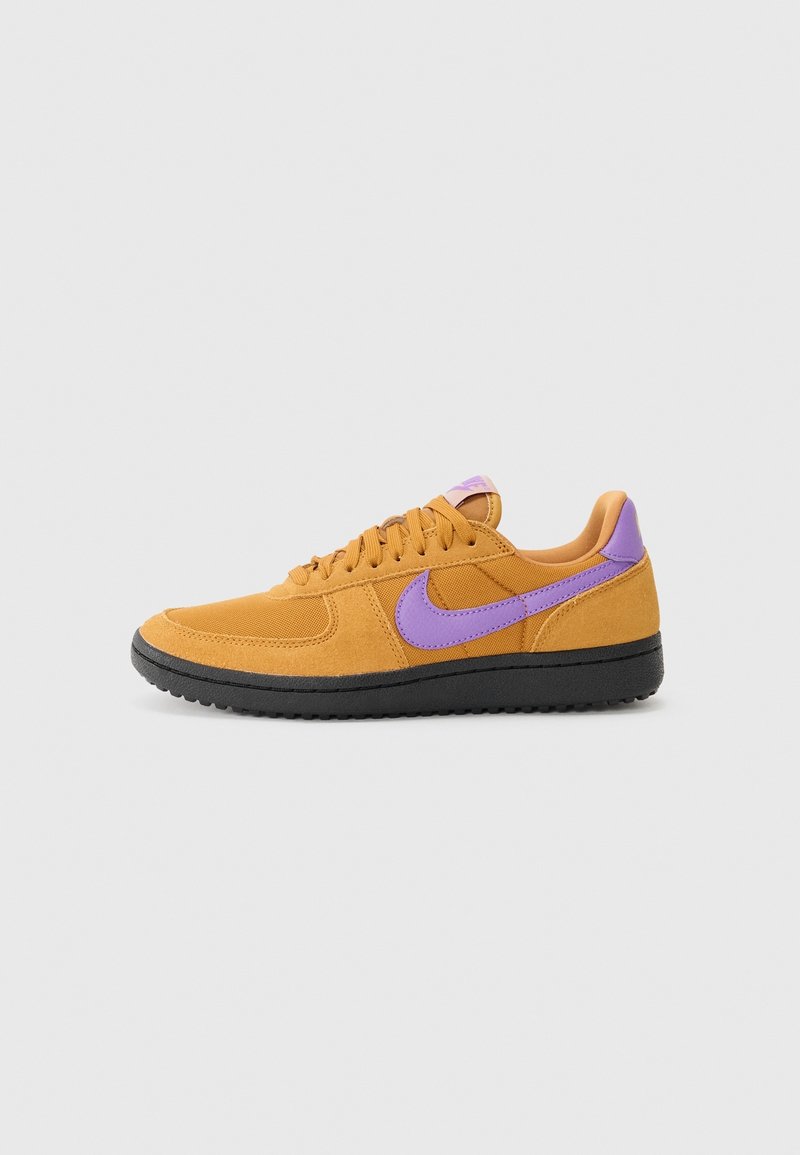 Baskets basses orange avec un swoosh Nike violet et un onglet talon, semelle noire et lacets orange sur un fond gris clair.