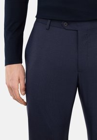 Navy pinstripe dress trousers with a smooth texture, featuring a button closure and a flat front design. Hand resting on the waist.