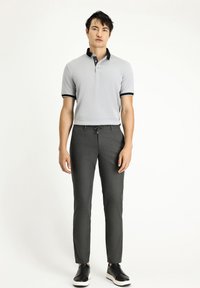 Lichtgrijze polo met zwarte accenten, korte mouwen, twee knopen, gecombineerd met donkergrijze slim-fit broeken en zwarte sneakers.