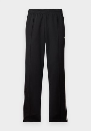 Pantalon de sport noir à longueur complète avec taille élastique et rayures blanches sur les côtés, arborant un petit logo vert sur le côté supérieur.