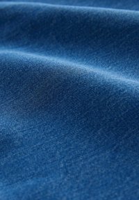 Niebieska tkanina dżinsowa z widoczną diagonalną fakturą tkania, ukazująca miękkie fałdy i naturalne odbicie światła.