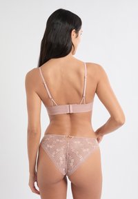 Spitzenwäsche-Set in zartem Rosa, bestehend aus einem BH mit verstellbaren Trägern und Häkchenverschluss, kombiniert mit einem passenden Tanga, der filigrane Blumenmuster zeigt.