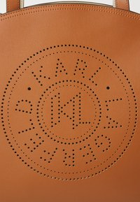 Borsa tote in pelle tan con design circolare perforato che presenta il testo "KARL" e "GERMANIA", completata da accenti rotondi in bold.