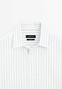 Chemise blanche à fines rayures verticales noires et col pointu, montrant l’étiquette intérieure portant la mention Massimo Dutti.