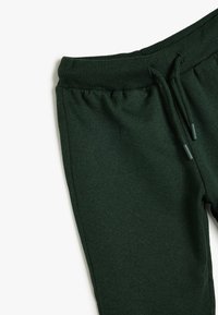 Pantalones de chándal verde oscuro fabricados con una suave mezcla de algodón. Presentan una cintura acanalada, cierre con cordón y una textura suave.