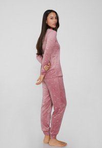 Rosa, samtige Pyjamas mit Tupfenmuster, bestehend aus einem Langarmoberteil und Hose im Jogger-Stil mit gerippten Bündchen, weiche Textur.