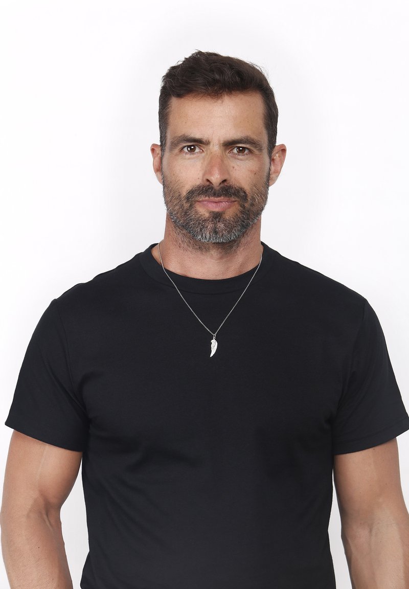 Camiseta de algodón negra de manga corta, con cuello redondo. Accesorizada con un collar plateado que muestra un colgante en forma de pluma.