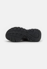 Sneaker nera con una suola in gomma testurizzata caratterizzata da scanalature profonde e motivi in rilievo per una maggiore presa. Dettaglio del logo circolare sul tallone.