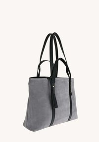 Sac fourre-tout en suède gris avec des poignées en cuir noir et des détails à frange, présentant une forme rectangulaire structurée et des accents en métal doré.