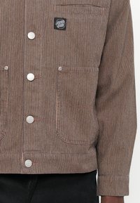 Gestreepte corduroy jas in bruin en beige met zilveren knopen, twee voorzakken en een zwart logo label op de bovenste linkerzijde.