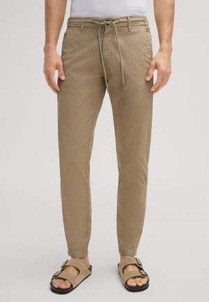 Lichtbruine broek met een trekkoord taille, taps toelopende pijpen en zijzakken. Gepaard met beige sandalen met twee zwarte gespen.
