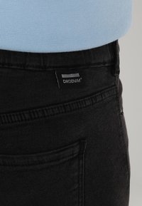 Schwarze Jeans aus Denim mit einem Etikett mit dem Markennamen "DRDENIM". Enthält eine Gesäßtasche und wird mit einem hellblauen Oberteil kombiniert.