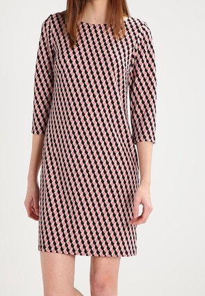 Vrouw draagt een knie-lange jurk met driekwart mouwen, voorzien van een geometrisch patroon in roze, zwart en wit.