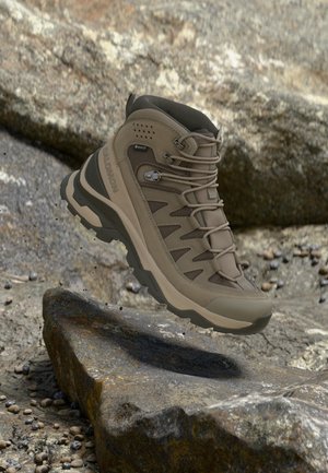 Bota de senderismo Salomon marrón con Gore-Tex, flotando sobre terreno rocoso, destacando su durabilidad y agarre resistentes para exteriores.