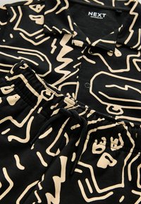 Chemise noire à col et pantalon assorti à taille élastique avec motifs linéaires abstraits beiges et détails de boutons sur le devant de la chemise.