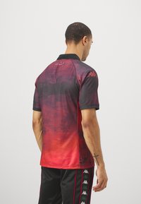 Polo shirt con gradiente rosso e nero, colletto, maniche corte e dettagli grafici discreti. Logo Kappa sulla spalla. Texture liscia.