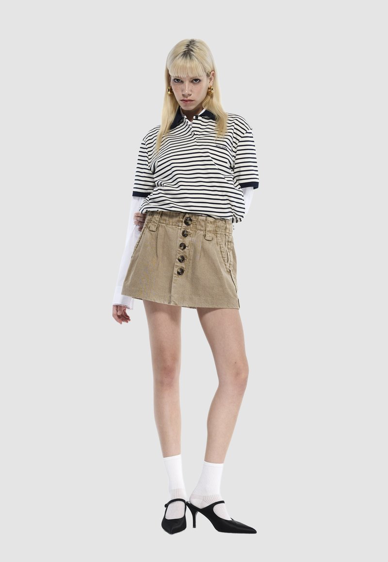 Striped polo shirt with short sleeves, beige skirt featuring front buttons, and black heels. White ankle socks accent the look.