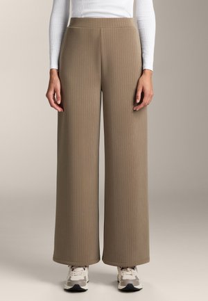 Wijd-uitlopende broek in ribbelstof in taupe met een zachte textuur. Voorzien van een elastische tailleband en valt tot de enkels. Gecombineerd met sneakers.