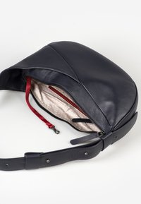 Borsa a tracolla in pelle blu navy con design curvo, interni rossi e chiusura con cerniera. Dispone di una tasca interna e di una tracolla staccabile.