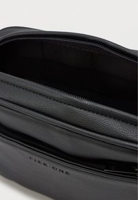 Melna ādas soma ar strukturētu virsmu, ar rāvējslēdzēja aizdari un gludu iekšējo odere. Smalks zīmols ir iepresēts priekšpusē.