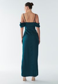 Teal satijnen avondjurk met een getailleerde silhouet, off-shoulder geplooide mouwen en een rits aan de achterkant. Vloerlange ontwerp en minimalistische hakken.