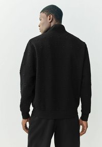 Sort tekstureret jakke med et hævet træmønster, ribbede manchetter og krave. Viser en slim fit med et rent, moderne design.