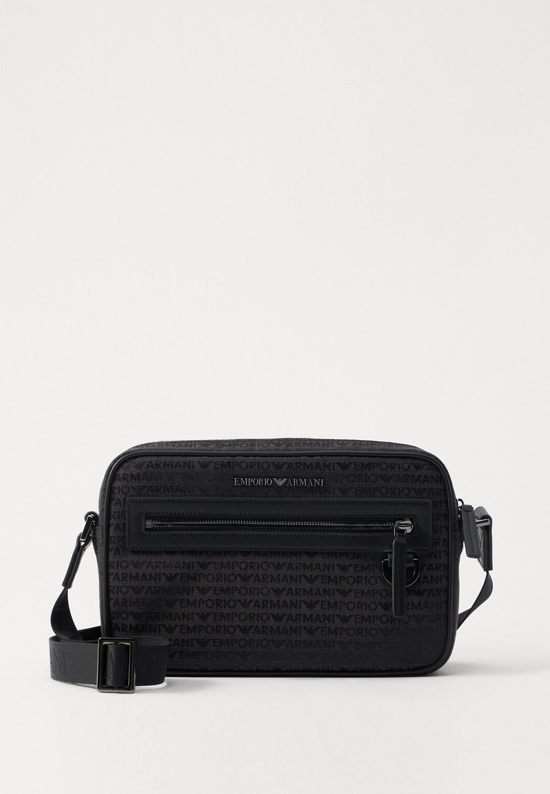Black crossbody bag made of textured fabric featuring a zippered front pocket, adjustable strap, and embossed logo accents.