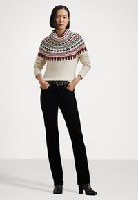 Maglione lavorato a maglia color crema con un motivo a yoke nero e rosso, abbinato a pantaloni di velluto a coste neri e stivali neri con tacco.