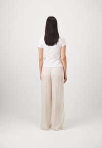 Vit t-shirt med kort ärm, kombinerad med ljusbeiga, fladdrande, vida byxor. Tyget verkar mjukt med en lös passform och subtil textur.