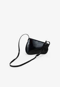 Bolso bandolera de cuero negro con forma curva, cierre de cremallera y una correa delgada ajustable para un uso versátil. Textura suave con detalles mínimos.
