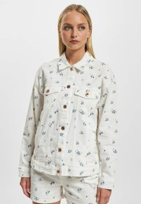 Hvit denimjakke med blå blomstermønster, store knapper og kragehals. Har frontlommer og en avslappet passform.