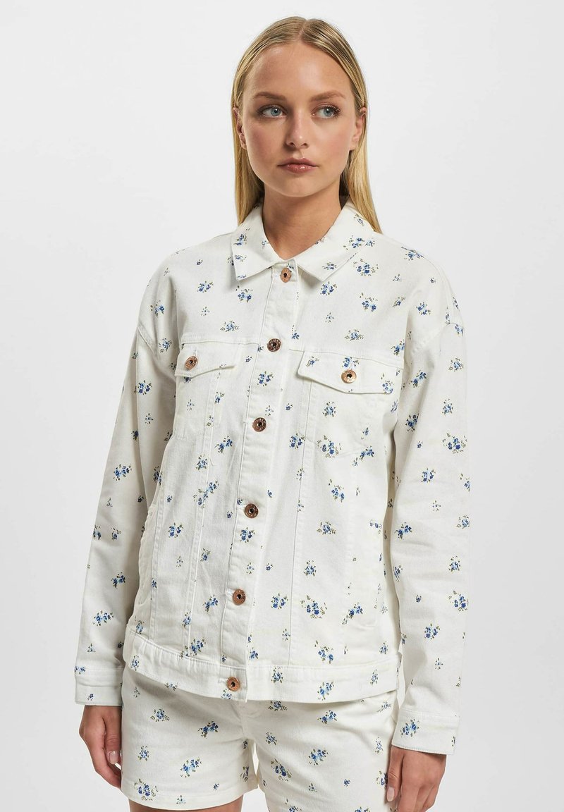 Hvit denimjakke med blå blomstermønster, store knapper og kragehals. Har frontlommer og en avslappet passform.