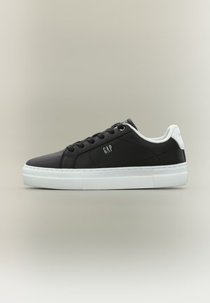 Baskets basses noires avec semelle blanche et languette au talon, lacets noirs, et logo "GAP" sur le côté.