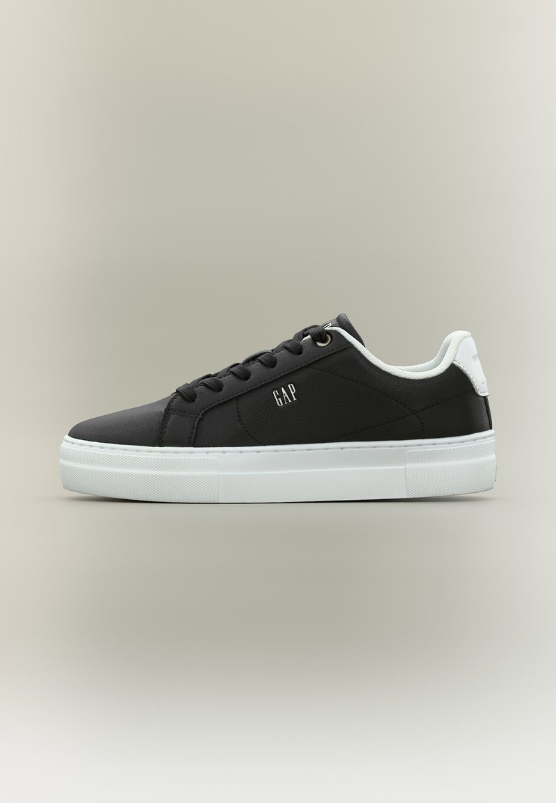 Baskets basses noires avec semelle blanche et languette au talon, lacets noirs, et logo "GAP" sur le côté.