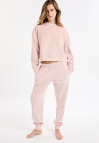 Ensemble de vêtements d'intérieur rose clair côtelé comprenant un haut court à manches longues et un pantalon à cordon avec poches latérales, confectionné en tissu doux.