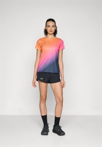 Kortärmad t-shirt med gradient från orange till marinblå, med en blommig design. Matchad med svarta shorts och träningsskor.
