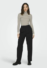 Black tailored wide-leg trousers paired with a ribbed cream and black striped turtleneck. Model stands against a light gray background.