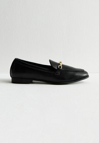 Mocasines de cuero negro con tacón plano, que cuentan con un acento de metal dorado en la parte delantera y un diseño suave y elegante.