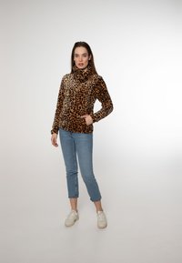 Giacca in pile con zip in stampa leopardata, colletto alto, maniche lunghe e tasche sul davanti, abbinata a jeans cropped blu chiaro e sneakers bianche.
