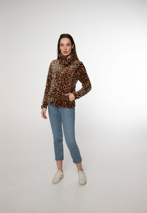Jakna od flisa s leopard uzorkom na zip, s visokim ovratnikom, dugim rukavima i prednjim džepovima, u kombinaciji s svijetloplavim krojenim trapericama i bijelim tenisicama.